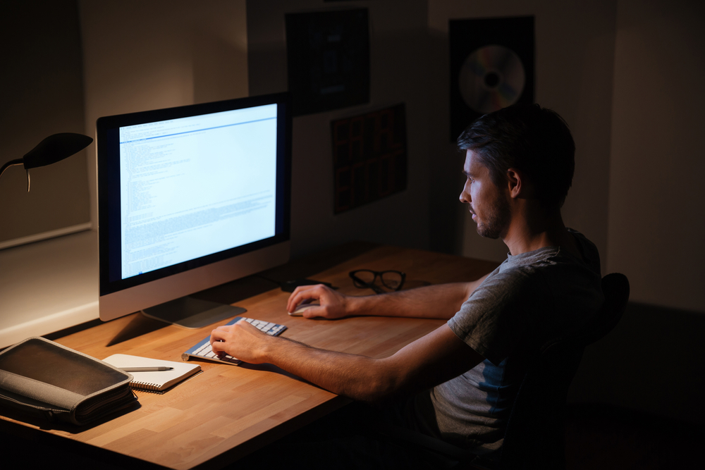 Handsome young man sitting in dark room and using computer Handsome young man sitting in dark room and using computer